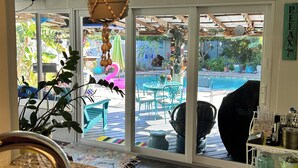 A kitchen with a granite countertop, a hanging macrame light fixture, and a view of an outdoor patio with a pool and outdoor furniture. - Sea Grape Escape Mid-Century Modern Pool home! (North Palm Beach)