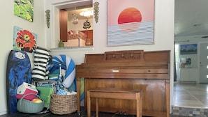 A room with a piano, a wicker basket, and a surfboard. - Sea Grape Escape Mid-Century Modern Pool home! (North Palm Beach)