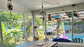 A dining area with a wooden table and chairs, a bench, and hanging plants. - Sea Grape Escape Mid-Century Modern Pool home! (North Palm Beach)