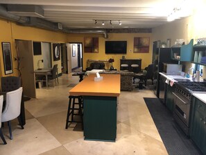 Una cucina con isola centrale, zona pranzo con sedie, un divano e una TV fissata al muro.