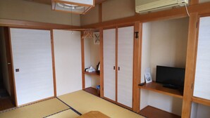 A traditional Japanese room with tatami flooring, sliding doors, a television on a wooden shelf, and a ceiling fan. - Resort House FURUSATO (Nozawaonsen)