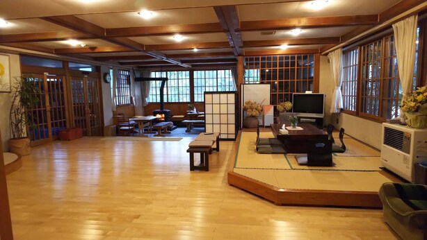 A traditional Japanese-style living room with tatami flooring, a low table, cushions, a television, and a fireplace. - Resort House FURUSATO (Nozawaonsen)