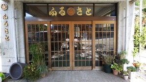 A building entrance with a large wooden door, potted plants, and a sign with Japanese characters. - Resort House FURUSATO (Nozawaonsen)