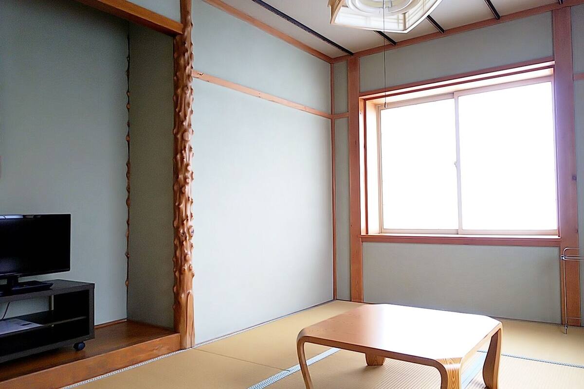 A room with tatami flooring, a television, a window, and a small cabinet.