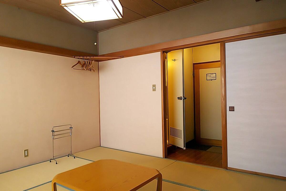 A room with tatami flooring, a low wooden table, a hanging rack, and a sliding door leading to another room.