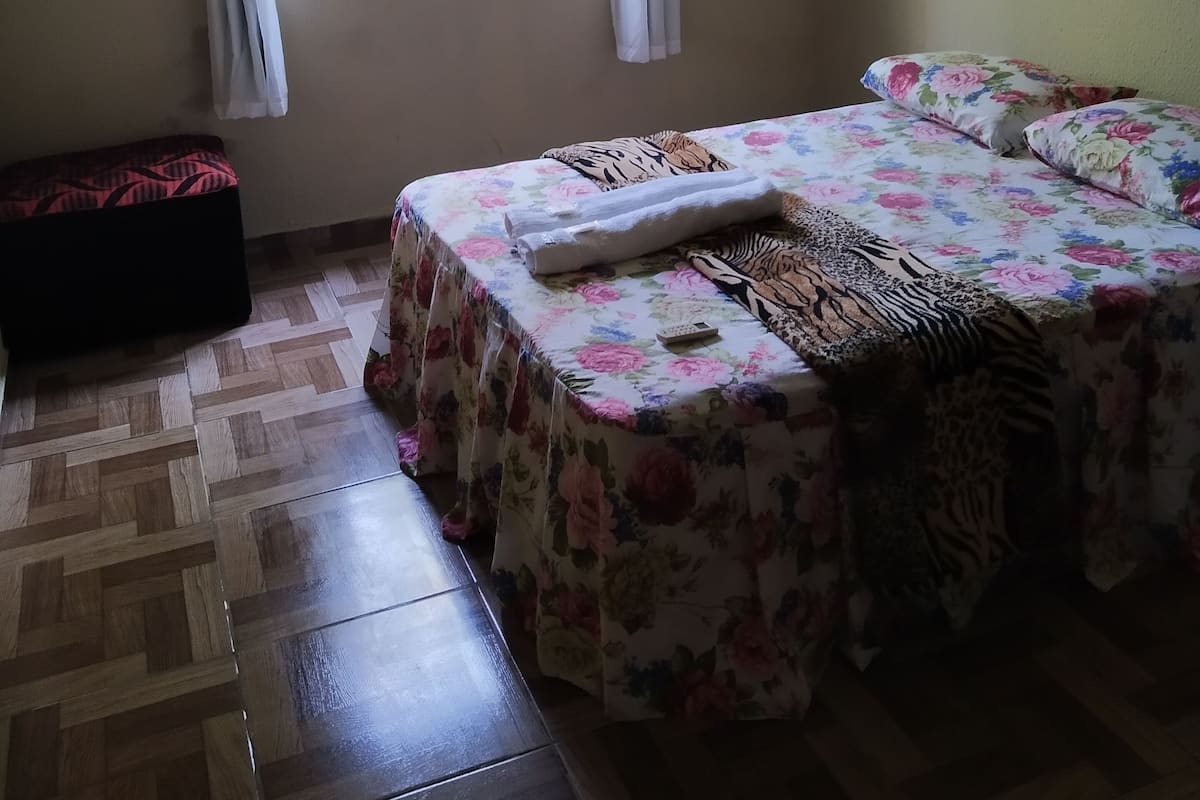 A bedroom with a bed, a bench, a window, and a view of greenery outside.