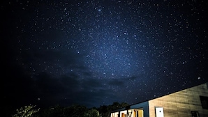 A night sky filled with stars above a modern building with large windows. - Ananda Chillage (Yakushima)