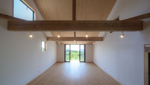 A spacious room with wooden beams, large windows, and a view of greenery. - Ananda Chillage (Yakushima)