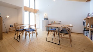 A spacious room with wooden flooring, a dining table with chairs, a bookshelf, and a window providing natural light. - Ananda Chillage (Yakushima)
