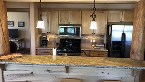 A kitchen with wooden cabinets, a granite countertop, a stove, a microwave, and a refrigerator.