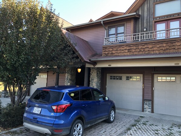 A blue SUV parked in front of a house with a stone facade, a balcony, and two garage doors.