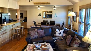A spacious living area with a dark brown leather sofa, wooden bar counter, and a dining area with a stone fireplace.