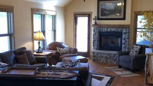 A cozy living room with a fireplace, a chandelier, and a large window.