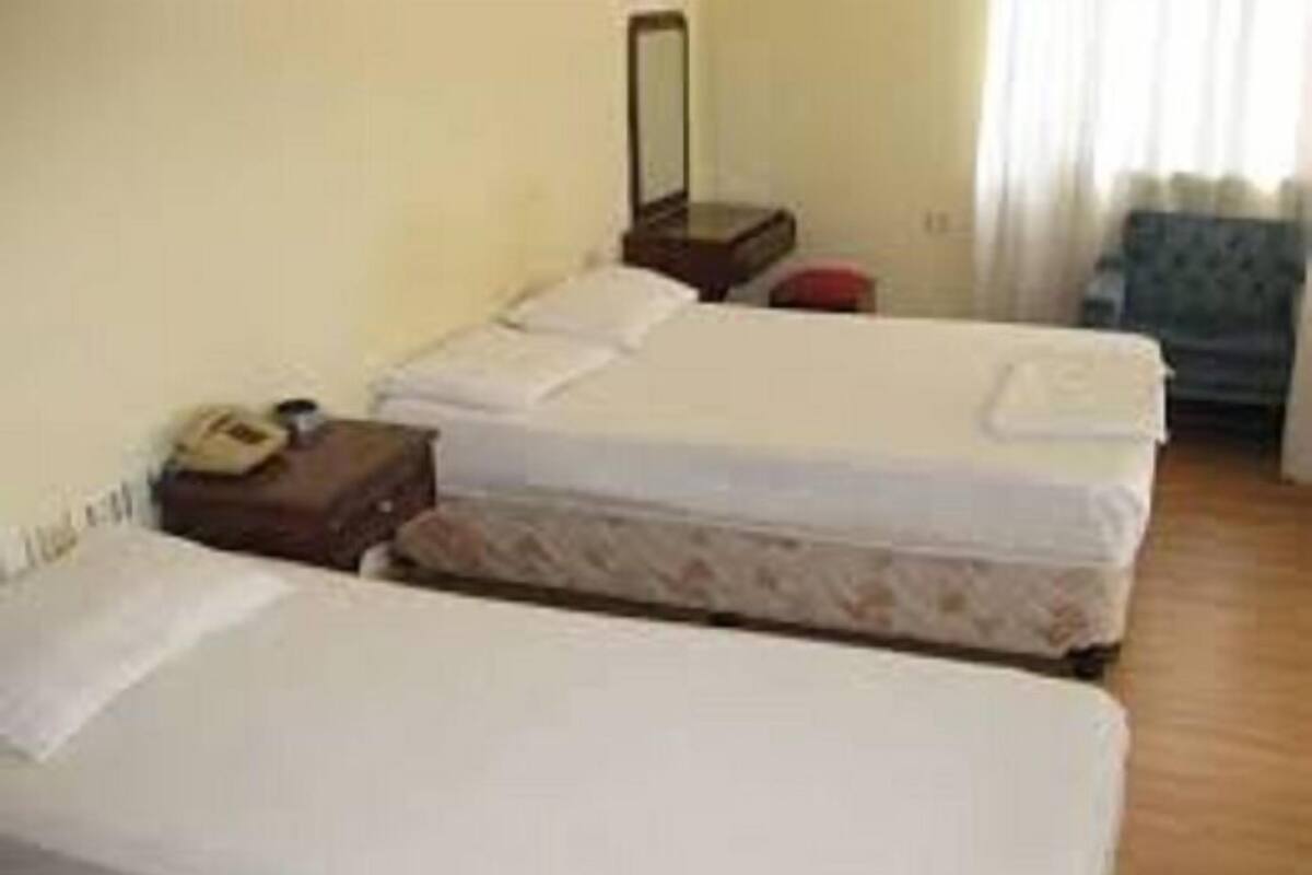 A hotel room with two single beds, a bedside table with a lamp, a chair, and a window with curtains.