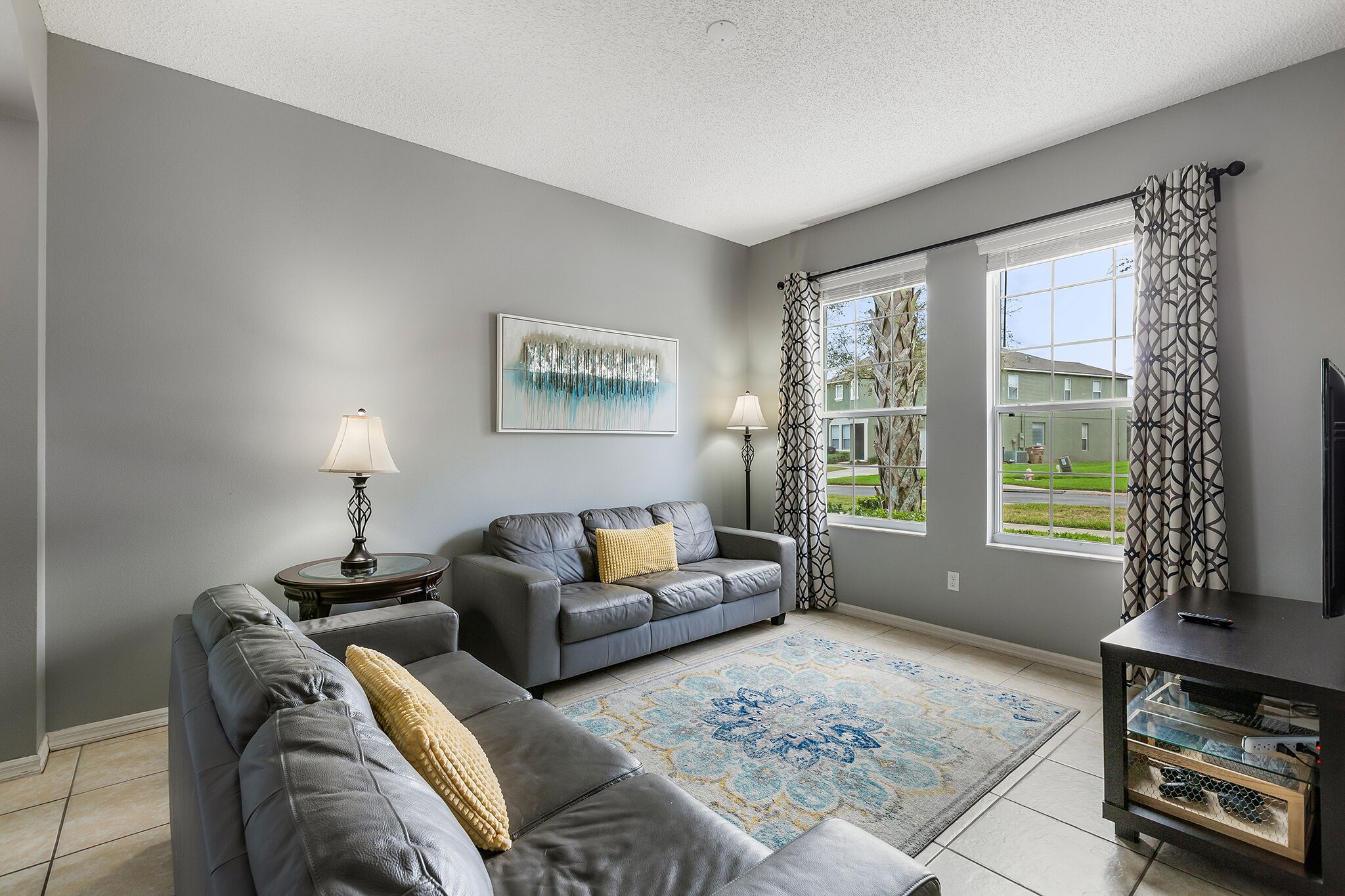 A living room with grey sofas, a patterned rug, a painting, and a TV on a stand.