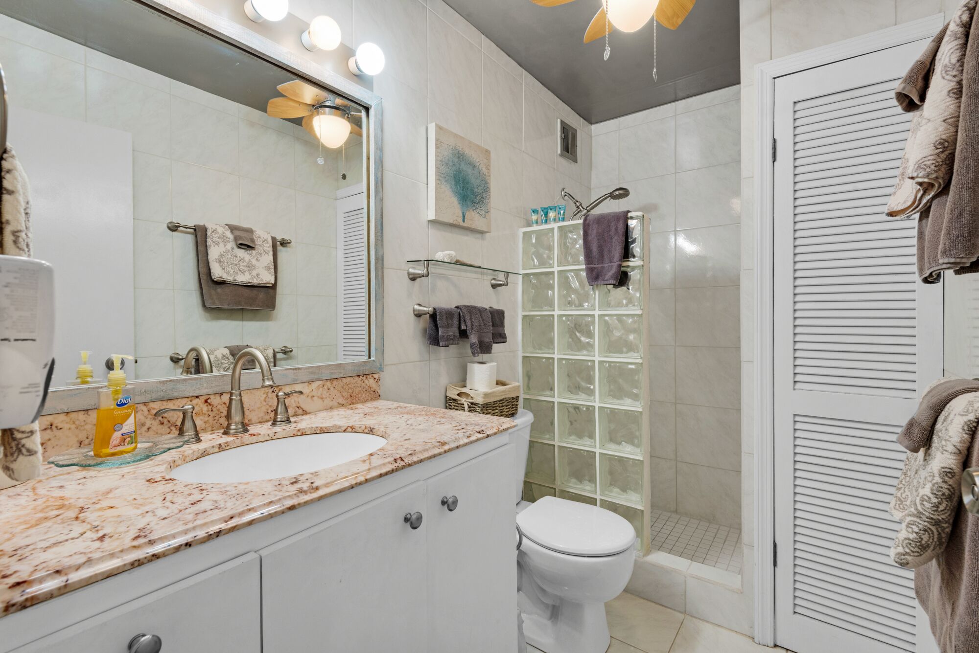 Un baño con lavamanos de mármol, inodoro, cabina de ducha de vidrio y espejo con iluminación.