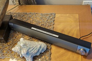 Un haut-parleur Bluetooth posé sur une surface en bois, avec un filet et un coquillage à proximité.