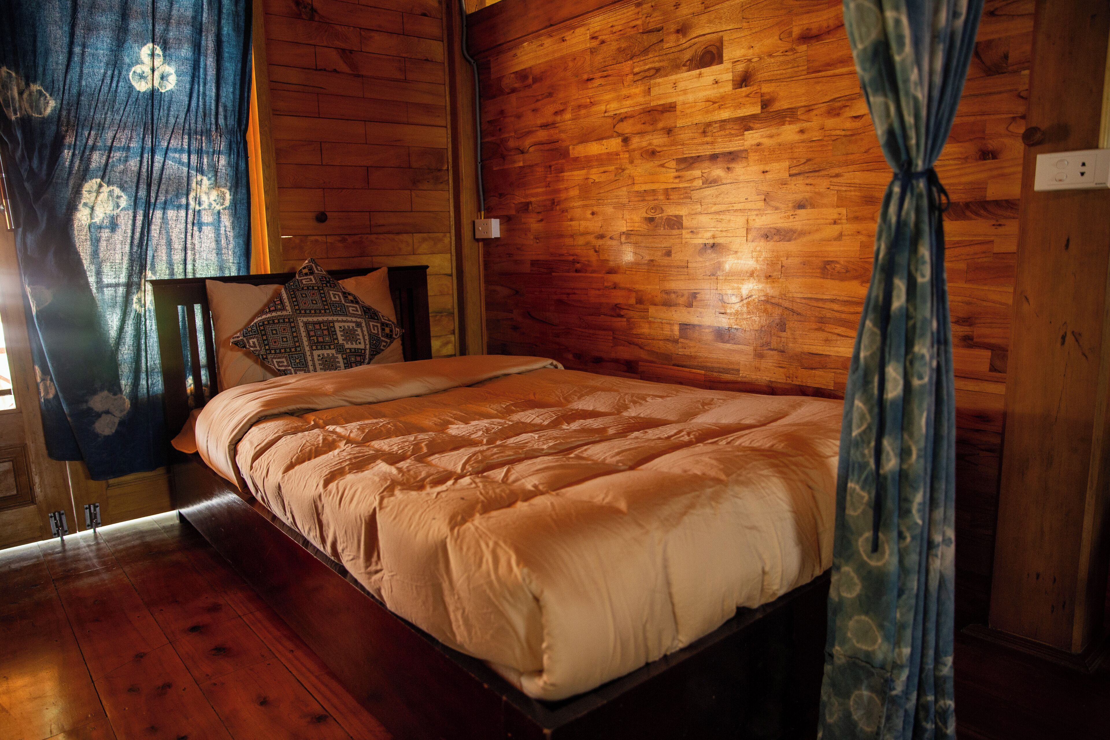 A wooden-paneled bedroom with a bed, curtains, and a wooden floor.