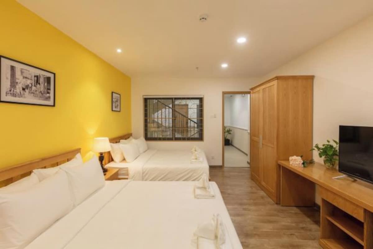 A hotel room with two beds, a wooden wardrobe, a television, and a window with a view of a staircase.