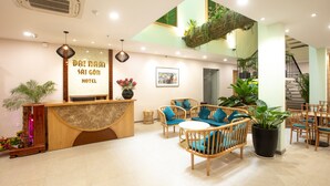 A hotel reception area with a wooden reception desk, wicker furniture, and a staircase leading to an upper level. - Dai Nam Sai Gon Hotel (Ho Chi Minh City)