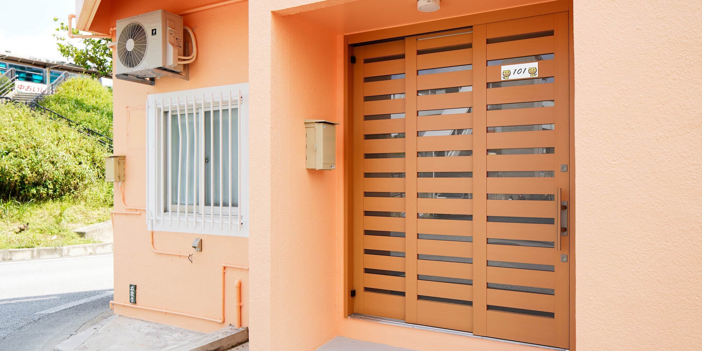 A building with a peach-colored exterior, a barred door with a sign, and an air conditioning unit on the wall.