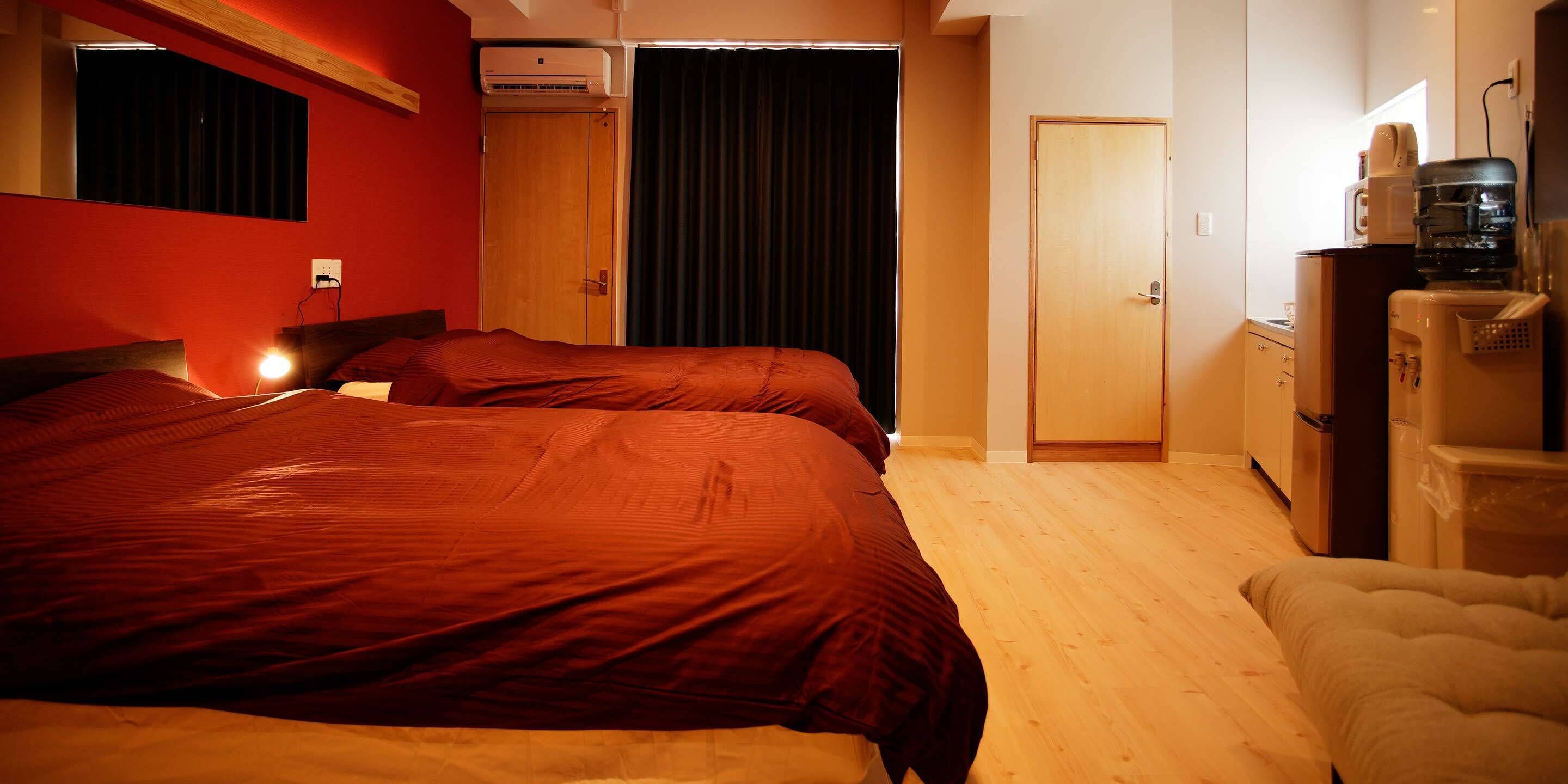 Een hotelkamer met twee bedden, een houten vloer, een kledingkast, een bureau met stoel en een kitchenette.