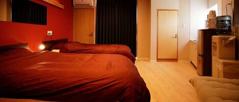 Een hotelkamer met twee bedden, een houten vloer, een kledingkast, een bureau met stoel en een kitchenette.