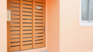 A wooden door with horizontal slats, a small sign above it, and a window with vertical blinds to the right. - Mcity in Furujima (Naha)