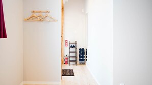 A hallway with wooden hangers on the wall, a fire extinguisher, and a shoe rack with multiple pairs of shoes. - Mcity in Furujima (Naha)