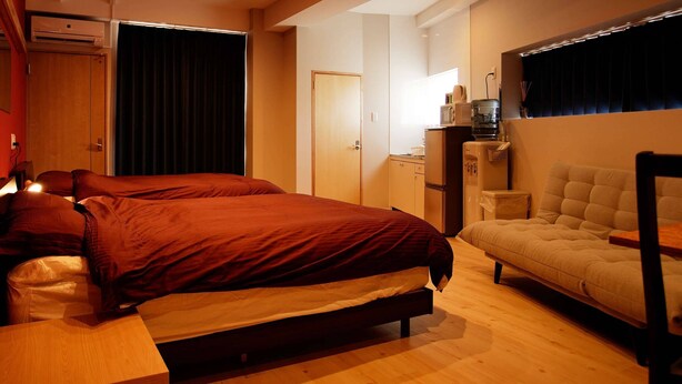 A bedroom with a bed, a sofa, a desk, and an air conditioning unit. - Mcity in Furujima (Naha)
