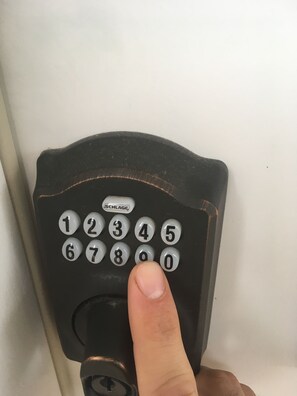 Primer plano de un teclado numérico en una cerradura, con un dedo pulsando el número 5.