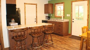 A kitchen with wooden cabinets, a refrigerator, a sink, and a dining area with a table and chairs. - Trailhead Suites (Marysville)