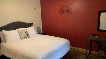 A bedroom with a bed, a ceiling fan, a wall-mounted bicycle illustration, a desk, and a chair.