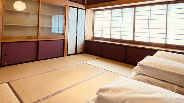 Une pièce de style japonais traditionnel, avec un sol recouvert de tatamis, un futon servant de lit, des portes coulissantes et une grande fenêtre à carreaux.