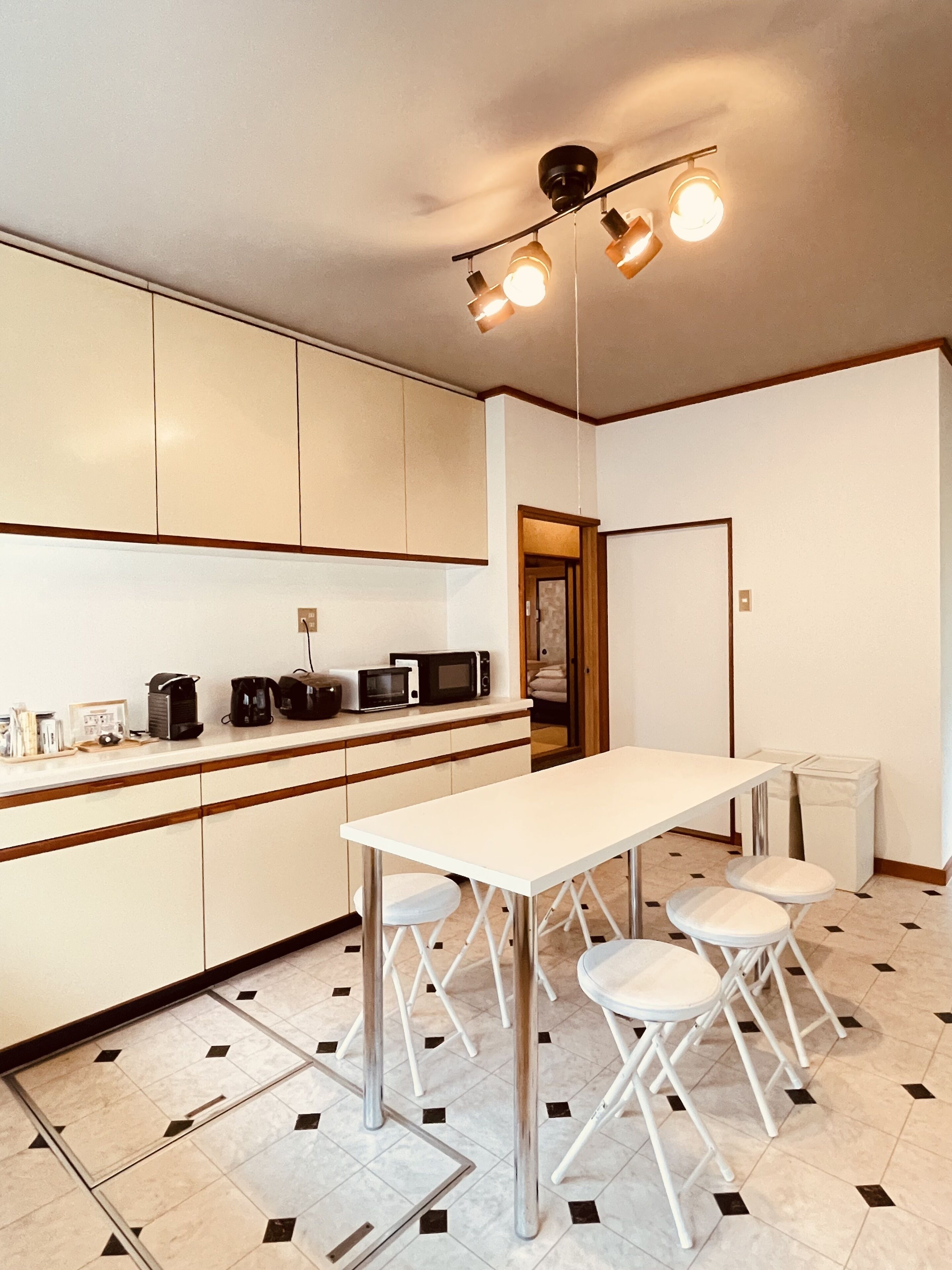 Una cocina compacta con encimera blanca, una mesa de comedor con cuatro taburetes y una lámpara en el techo.