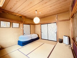 Una habitación japonesa tradicional con suelo de tatami, una cama con ropa de cama blanca, una lámpara de techo y puertas correderas.