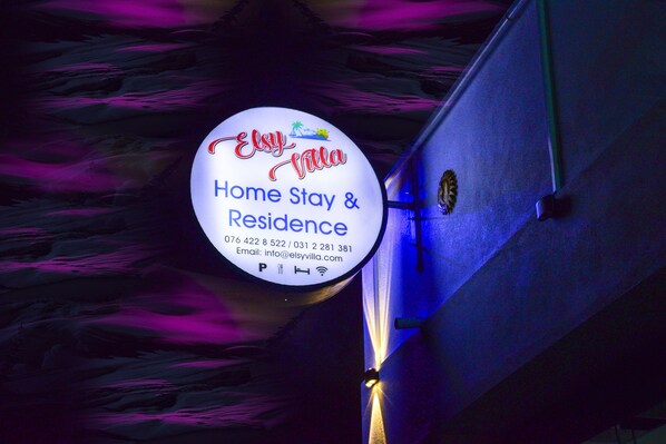 Un panneau circulaire portant l’inscription « Elsy Villa Home Stay & Residence » et les coordonnées.