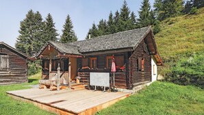 Een rustieke houten chalet met een houten terras, omringd door groen en bomen.