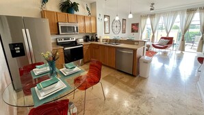 A modern kitchen with stainless steel appliances, wooden cabinets, and a dining area with a glass table and red chairs. - Steps from clubhouse.  "Be Our Guest" in Windsor Hills-pool heat included (Kissimmee)