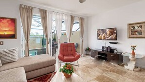 A modern living room with a sofa, a red chair, a TV, and a glass coffee table. - Steps from clubhouse.  "Be Our Guest" in Windsor Hills-pool heat included (Kissimmee)