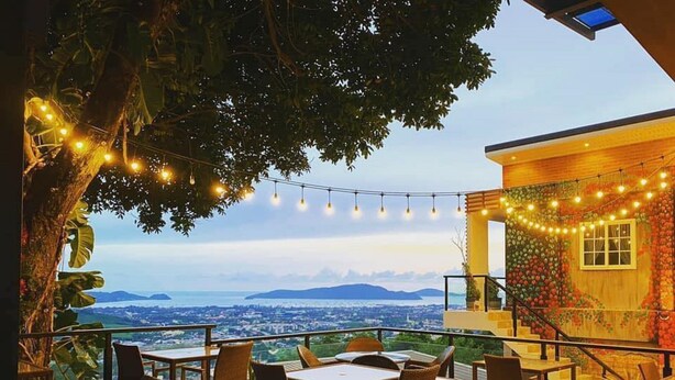 An outdoor dining area with tables and chairs, string lights, and a view of the city and mountains. - Phuket View Coffee and Resort (Chalong)