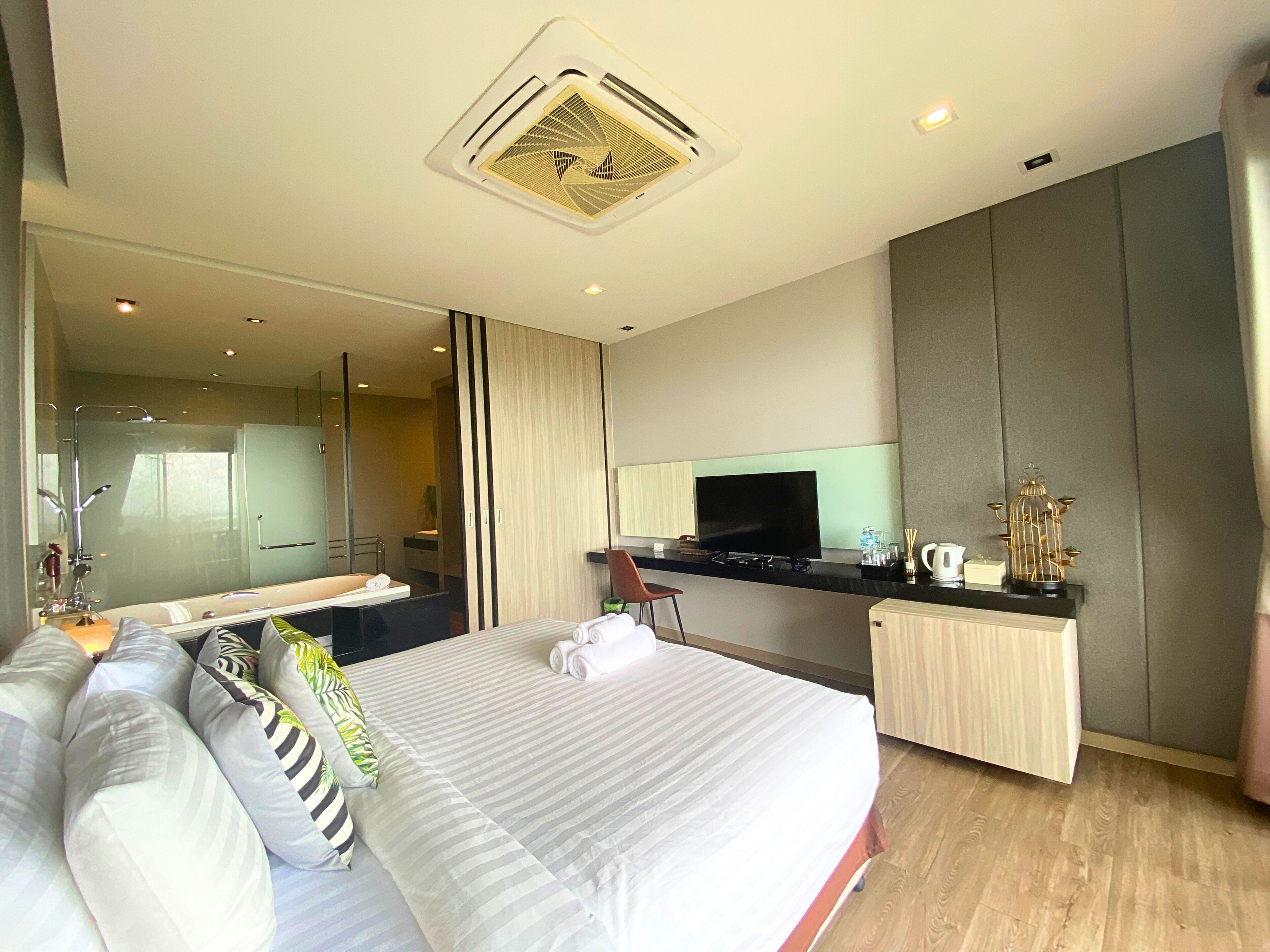 A modern hotel room with a large bed, a desk, a flat-screen TV, and a minibar.