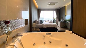 A modern hotel room with a large bathtub, a bed with a view, and a balcony with a railing. - Phuket View Coffee and Resort (Chalong)