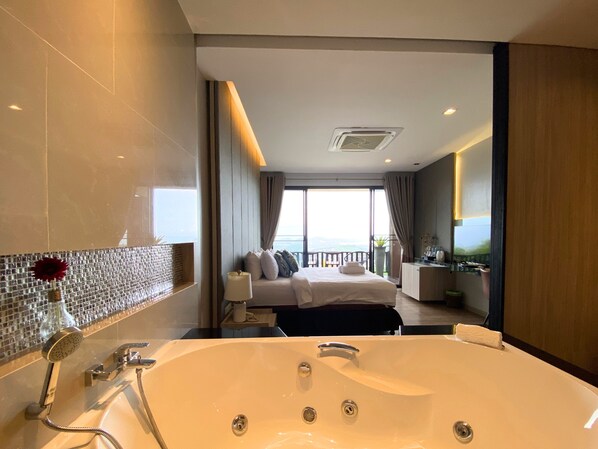 Una habitación de hotel moderna con una bañera grande, una cama con vistas y un balcón con barandilla.