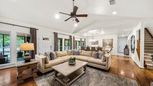 A spacious living room with a large sectional sofa, a coffee table, and a ceiling fan. - The Live Oak Haus (Sleeps 19) - 6 Bed | 6 Bath | Pool + Hot Tub + Fire Pit (Fredericksburg)