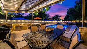 An outdoor patio with a covered seating area, a barbecue grill, and a pool. - The Live Oak Haus (Sleeps 19) - 6 Bed | 6 Bath | Pool + Hot Tub + Fire Pit (Fredericksburg)