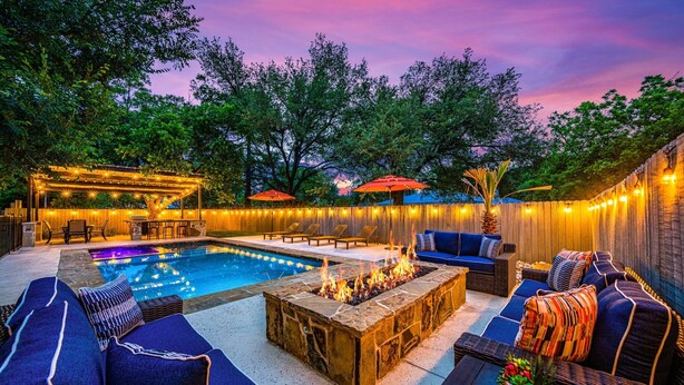 An outdoor pool area with lounge chairs, a fire pit, and string lights. - The Live Oak Haus (Sleeps 19) - 6 Bed | 6 Bath | Pool + Hot Tub + Fire Pit (Fredericksburg)
