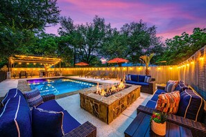 An outdoor pool area with lounge chairs, a fire pit, and string lights.