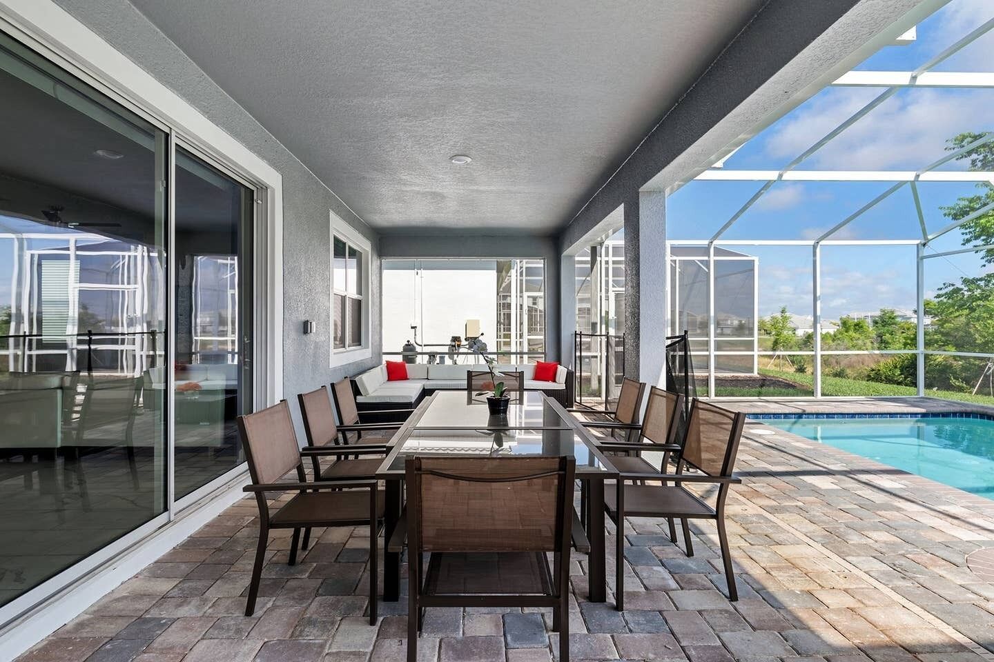 An outdoor patio with a glass-enclosed dining area, a pool, and a view of the surrounding landscape.