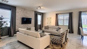 Een moderne woonkamer met een bank, fauteuils, een salontafel en een televisie aan de muur.